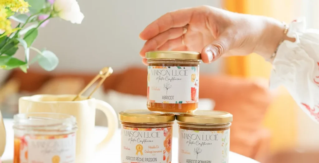Une main dépose un pot de confiture d'abricots sur un trio de pots placés l'un au-dessus de l'autre sur une table