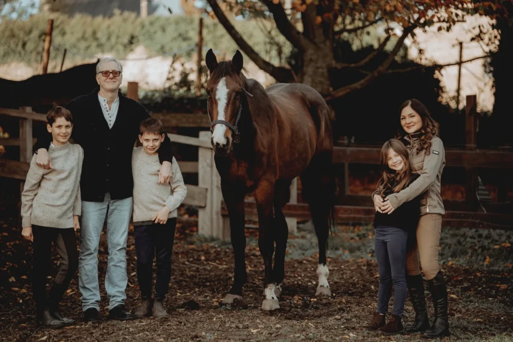 Groupe de deux adultes et quatre enfants posant avec un cheval dans une ferme en automne.